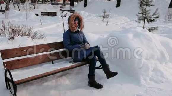 白天在大雪纷飞的天气里女人坐在冬季城市公园的长凳上视频的预览图