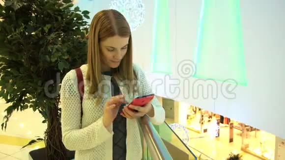 年轻漂亮的女人在商场里带着智能手机浏览互联网与朋友交流00359视频的预览图