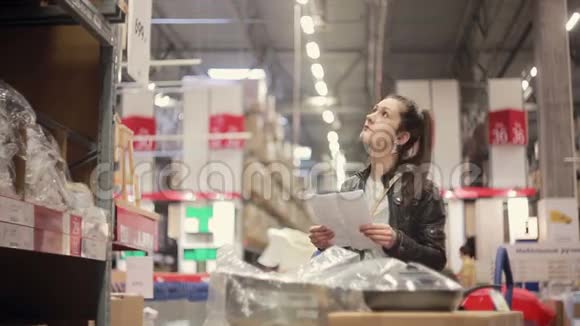 一个年轻的女人正在检查她的清单在货架上找东西把她的手推车推到仓库里视频的预览图