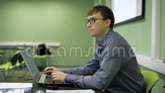 英俊的商人戴着眼镜坐在办公桌前在笔记本电脑上打字和观众交谈视频的预览图