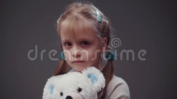 穿着一件米色毛衣有两条可爱辫子的欧洲小女孩手里拿着一个白色的泰迪熊看着镜头视频的预览图