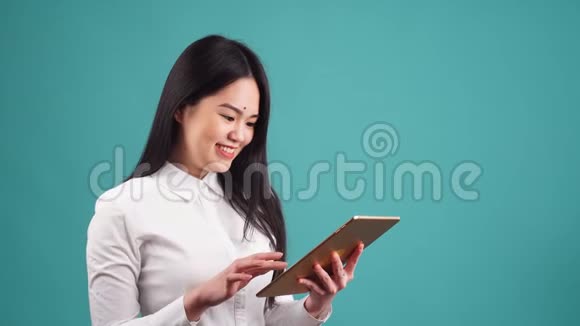 年轻的亚洲女孩在孤立的背景下使用平板电脑视频的预览图