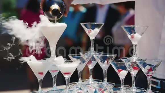 一个优雅的侍者用起泡的玻璃杯倒香槟从眼镜里喷出白烟和喷雾户外活动视频的预览图