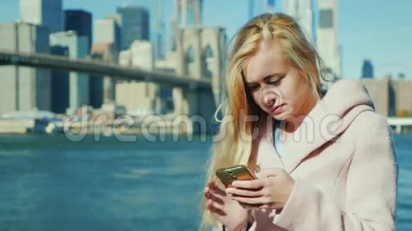 年轻女子在智能手机上打字在纽约布鲁克林大桥和曼哈顿天际线的背景下视频的预览图