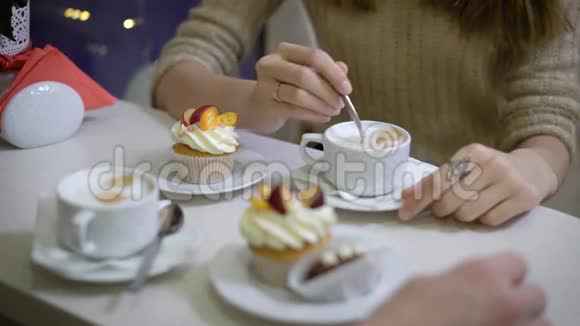 咖啡馆里的几个年轻人男孩和女孩去吃甜点卡布奇诺和纸杯蛋糕手的看法视频的预览图
