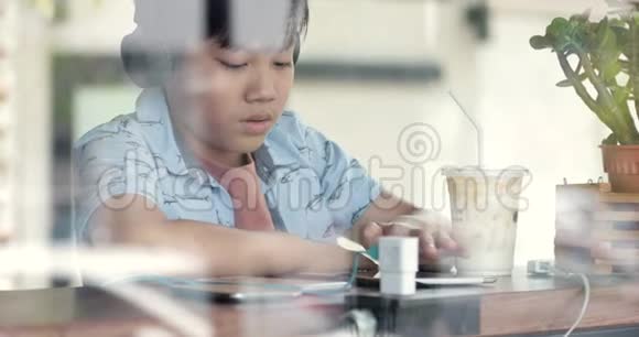 亚洲可爱的男孩用手机在杯子里喝牛奶微笑视频的预览图
