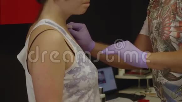 纹身艺术家戴着手套用棉垫擦拭女孩的皮肤准备纹身视频的预览图