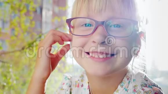 一个金发女孩的肖像对着镜头微笑听到音乐窗后有一棵绿树春天阳光明媚视频的预览图