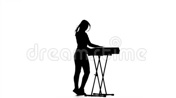 音乐家女孩在剪影中弹电子钢琴慢动作视频的预览图
