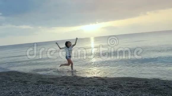 快乐的年轻女子在日落时在海滩上奔跑和跳舞视频的预览图