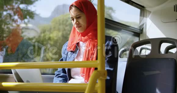 戴头巾的女人一边用笔记本电脑一边透过窗户看视频的预览图