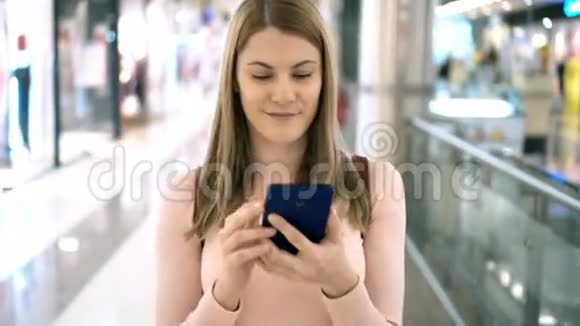 漂亮的女人带着智能手机在商场里散步浏览互联网与朋友交流视频的预览图
