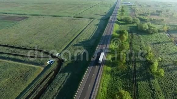 4K载有一辆卡车在太阳升起的绿野之间的道路上行驶的画面视频的预览图