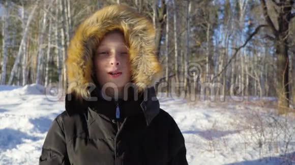 一个十几岁男孩的特写男孩微笑流露出情感阳光明媚的冬天晚上在森林里大风慢动作视频的预览图