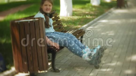 坐在长凳上听音乐的小胖女孩在公园里穿着溜冰鞋视频的预览图