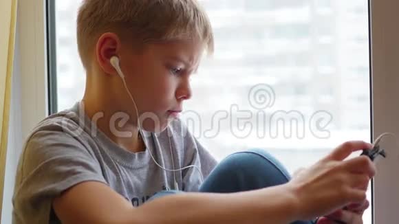孩子坐在窗台上用耳机特写在智能手机上听音乐视频的预览图