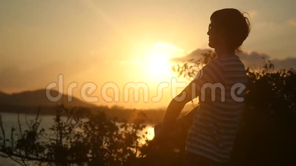 在山顶上美丽的夕阳下戴着墨镜的年轻人慢慢地举起双臂迎着朝阳视频的预览图