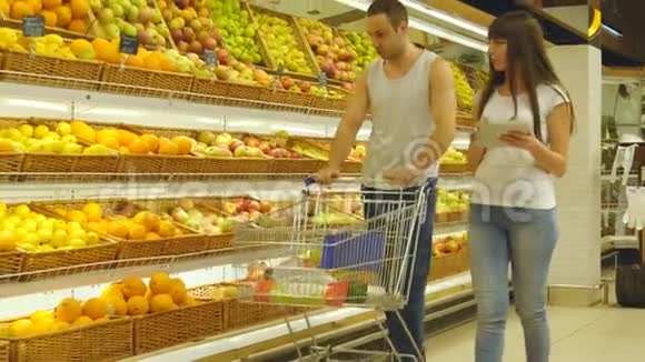 年轻的白种人夫妇带着市场手推车在超市里散步选择新鲜的苹果男人在放水果视频的预览图