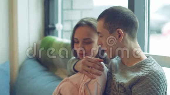 美丽的年轻夫妇带着愉快的谈话轻轻地拥抱坐在窗前视频的预览图