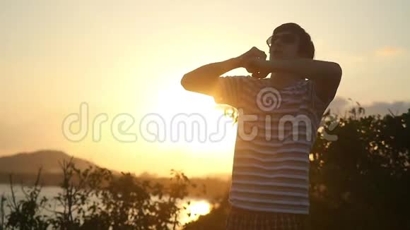 年轻人戴着太阳镜在美丽的夕阳下举起双臂慢吞吞地站在山顶上1920x1080个视频的预览图