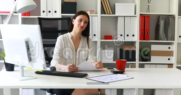 穿着白衬衫的女商人坐在桌边看着摄像机视频的预览图