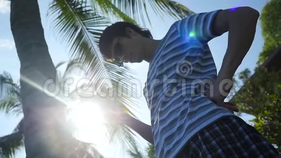 年轻人戴着太阳镜在室外使用移动智能手机在棕榈树下使用太阳和激光照明效果慢慢视频的预览图