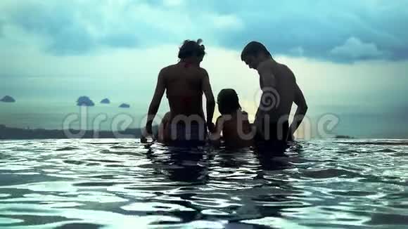 妈妈爸爸和他们的儿子坐在水池边在山顶上看到无限的海景动作缓慢并显示视频的预览图