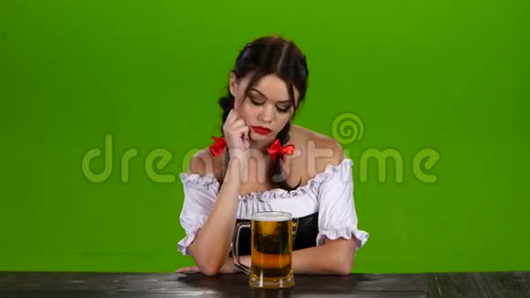 穿着巴伐利亚服装的女孩坐在桌边喝啤酒绿色屏幕视频的预览图