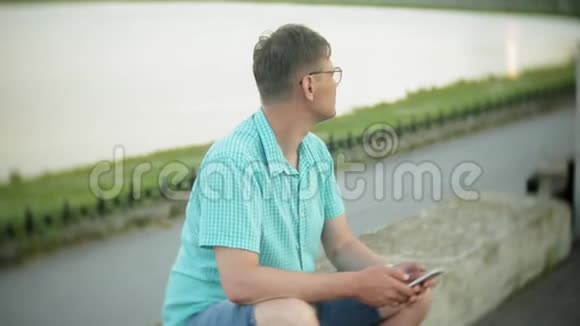 城市公园里有智能手机的年轻人坐在岸边视频的预览图