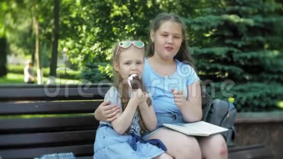 两个小女孩坐在一个城市的木凳上看书吃冰激凌这是一个城市的背景视频的预览图