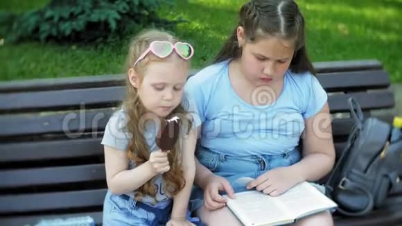 两个小女孩坐在一个城市的木凳上看书吃冰激凌这是一个城市的背景视频的预览图