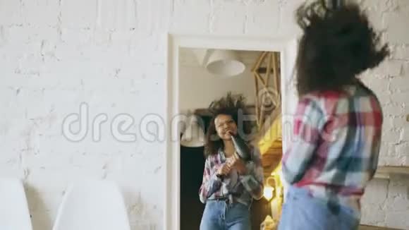 滑稽可笑的非裔美国女孩在家里用吹风机在镜子前跳舞唱歌视频的预览图