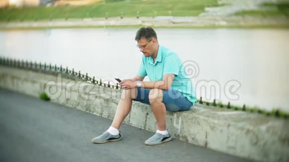 城市公园里有智能手机的年轻人坐在岸边视频的预览图