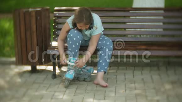 坐在长凳上听音乐的小胖女孩在公园里穿着溜冰鞋视频的预览图