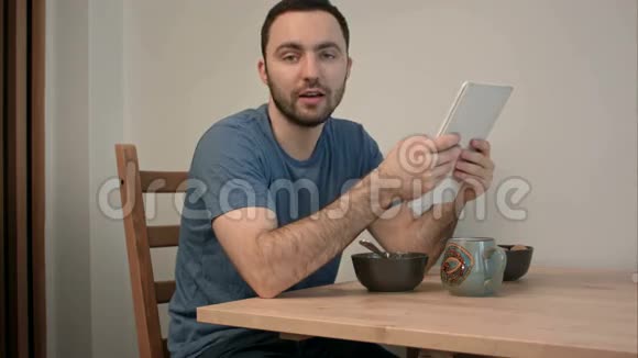 一个人在吃早餐的时候用数码平板电脑和摄像机说话视频的预览图