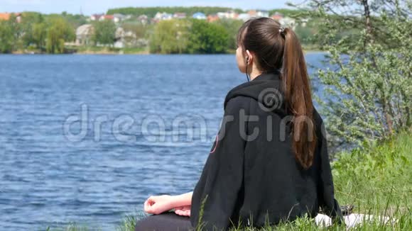 年轻女子脱下夹克享受阳光和温暖女孩坐在草地上在海滩上放松冥想视频的预览图
