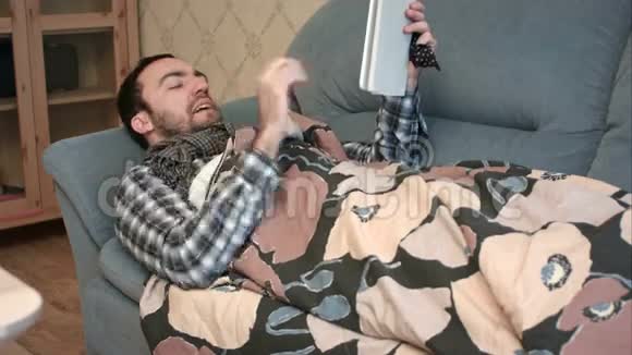 生病的年轻人用平板电脑躺在沙发上视频的预览图