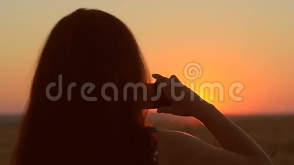 女孩带着手机在日落图上打着电话夕阳美丽的黄昏景观视频的预览图