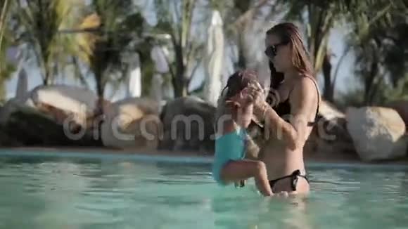 年轻的妈妈和可爱的小女孩在夏天的游泳池里玩视频的预览图
