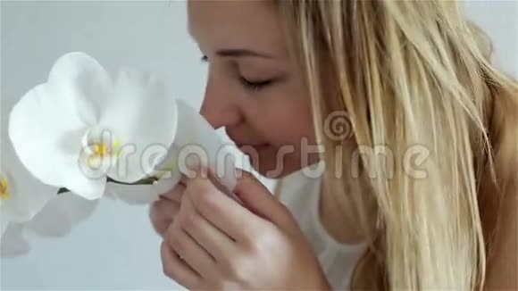 美丽的年轻女子闻着白色的兰花用手指抚摸着花瓣视频的预览图