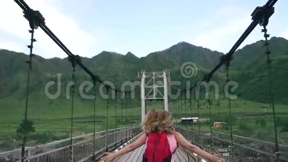 带背包的女旅行者沿着桥跑山区背景下的女游客慢动作视频的预览图