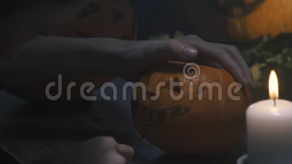 一个女人的手在万圣节南瓜上用一个木勺用刀子剪出一个杰克灯笼的微笑在木桌上视频的预览图