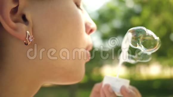 小女孩近距离吹肥皂泡慢动作春天夏天美丽的女孩在公园里吹肥皂泡视频的预览图