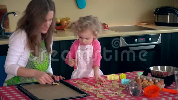 美丽的母亲和可爱的小女儿女孩把饼干放在烤箱锡里视频的预览图