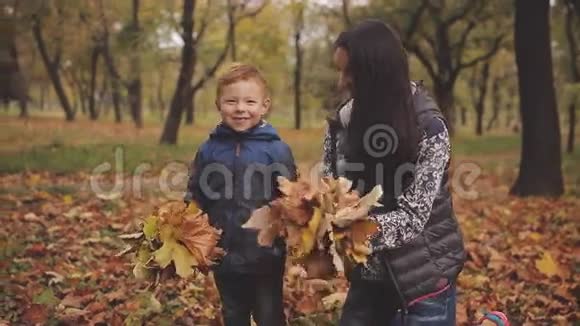 快乐的红头发的小男孩和他的母亲在秋天公园里呕吐黄叶视频的预览图