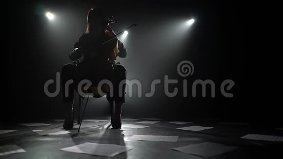女孩在地板上弹大提琴上的构图是分散的床单和音符剪影黑烟背景视频的预览图
