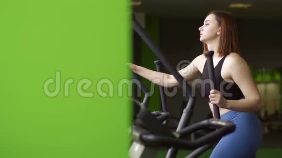 在绿色健身俱乐部的椭圆训练器上这位女士的侧面特写肖像使她的肌肉变美视频的预览图