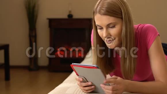 美丽迷人的年轻女子平板电脑躺在沙发上浏览互联网和微笑00333视频的预览图