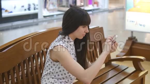 玩口袋妖怪的年轻女子在购物中心用智能手机进入室内坐在板凳上玩大众游戏的女孩视频的预览图