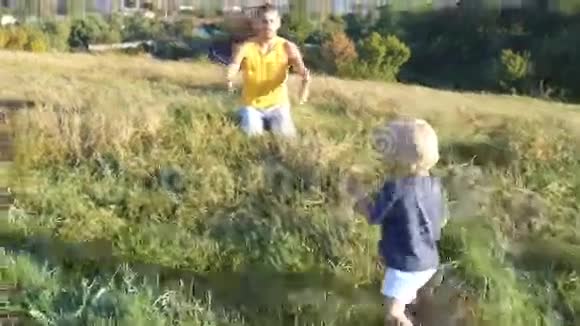 在阳光明媚的日子里小孩子在田野上给他的父亲吃青草爸爸在大自然中举起他的小男孩快乐视频的预览图